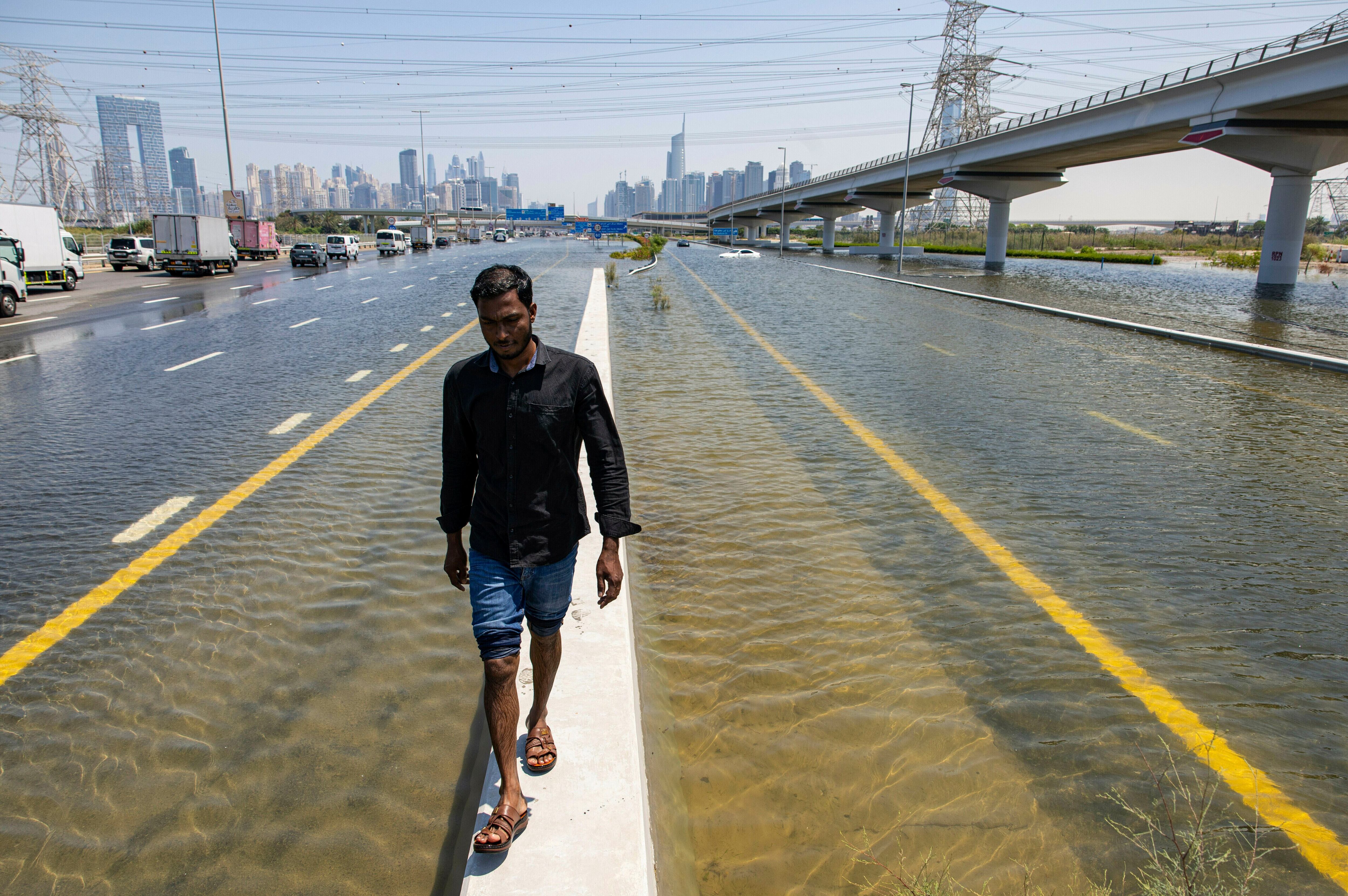 A man walks along a road barrier on Dubai's Sheikh Zayed Road amid floodwater caused by heavy rain, Thursday.