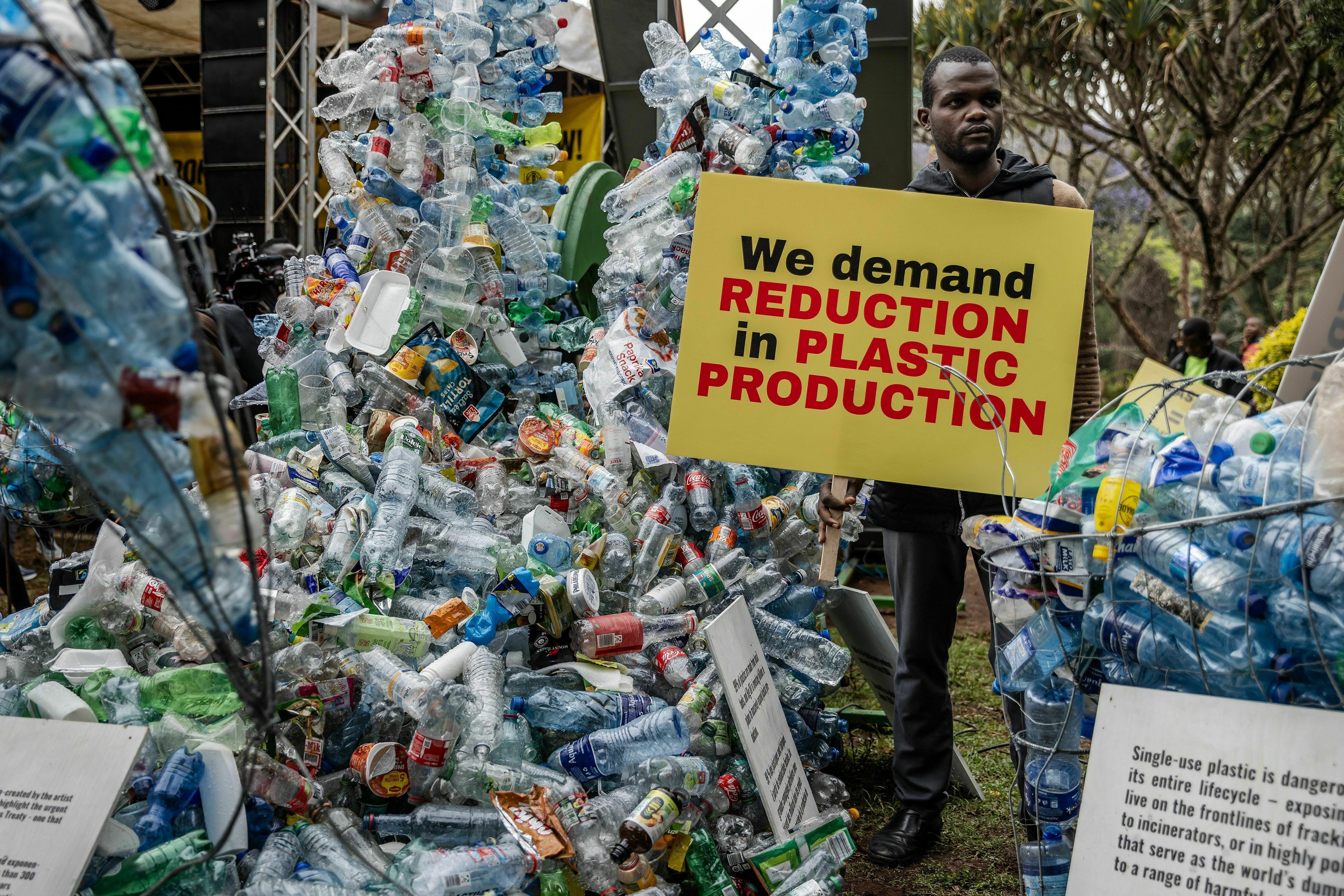 A climate activist holds a banner next to a plastic installation after marching to demand reductions in global plastic production ahead of negotiations in Kenya in November 2023.