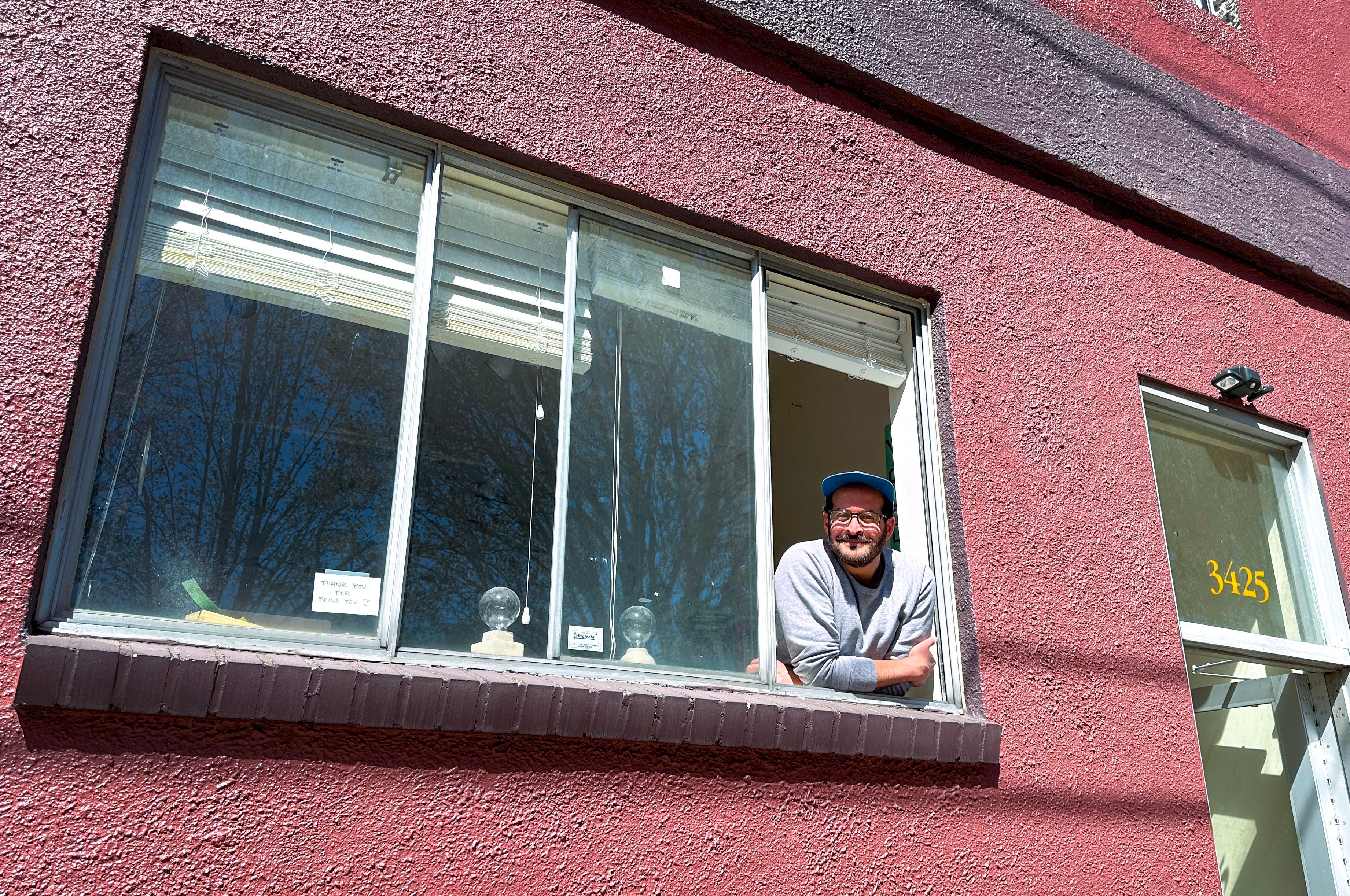 Anis Mojgani leans out the window of his Portland studio on April 17, 2024. He sometimes does poetry readings here at sunset.